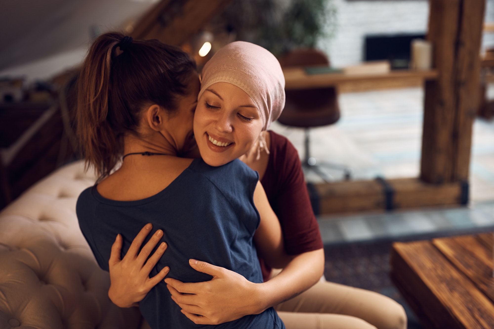 Happy cancer patient embracing her friend who is visiting her at home.